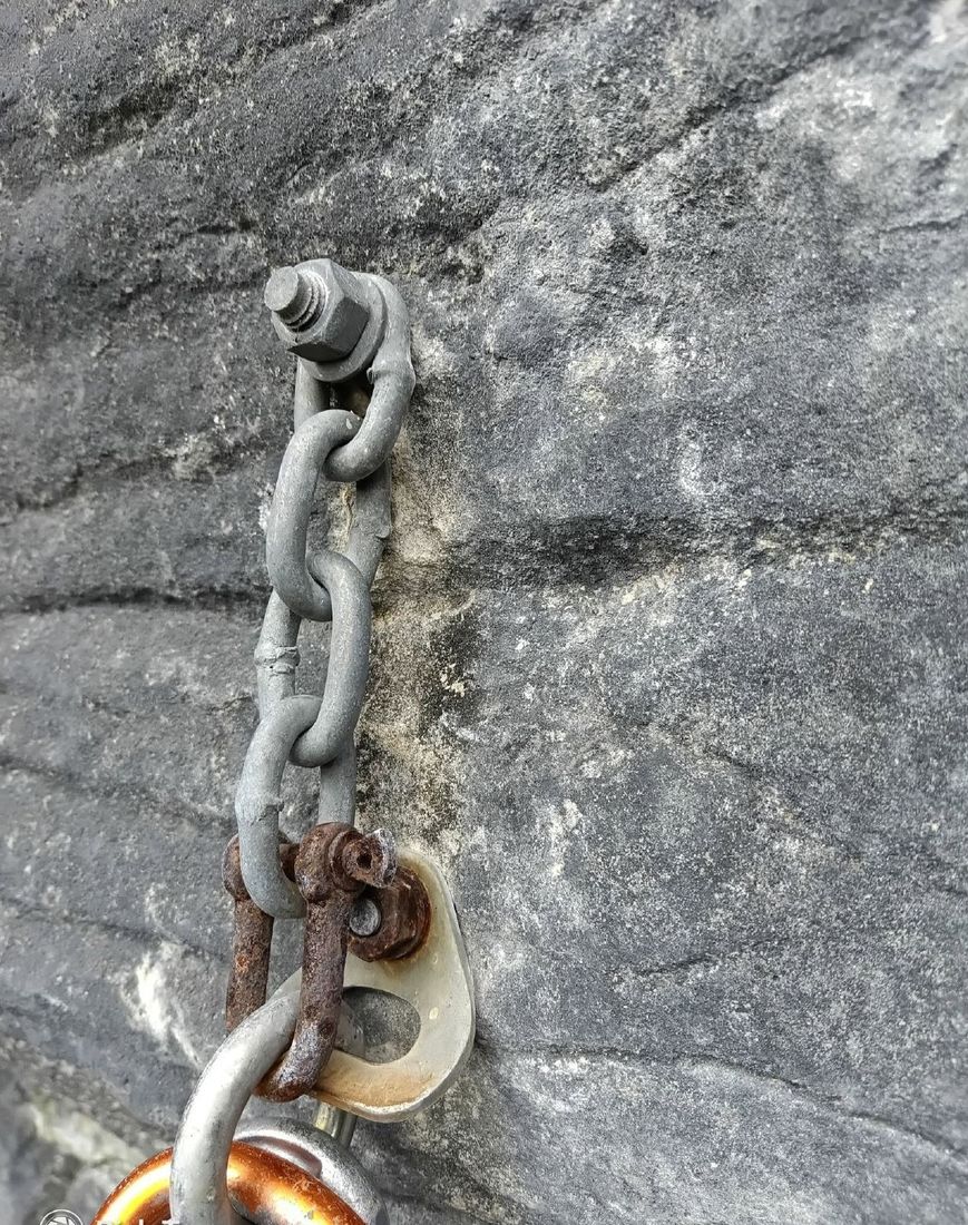 An old anchor with galvanised chain rusting through at the bolt